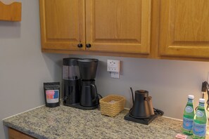 A kitchen with wooden cabinets, a coffee maker, a basket, and two bottles of Pellegrino water. - 4BD Hygge Home w/ Theater, Game Room & Workspace (Minneapolis)