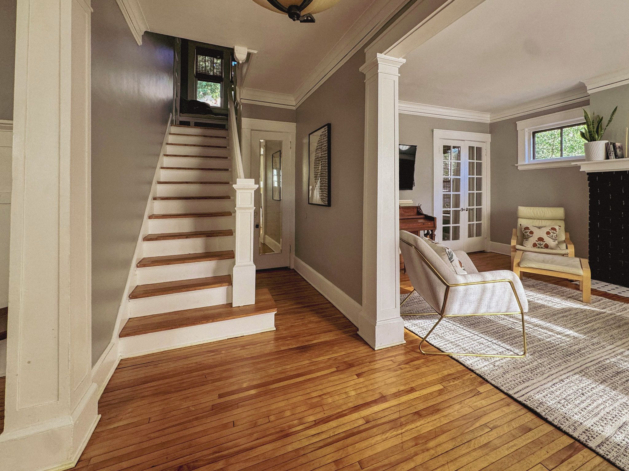 A staircase leading to a second floor, a living room with a sofa and a chair, and a fireplace.