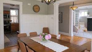 A dining room with a wooden table, chairs, a vase of flowers, a chandelier, and a clock on the wall. - 4BR Hygge Home | Theater + Game Room | Sleeps 10 (Minneapolis)