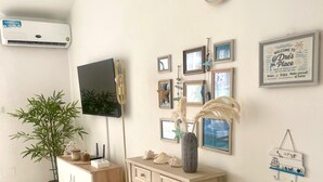 Ein Zimmer mit einem Flachbildfernseher, einem Holztisch, einer Topfpflanze und einer Wand-Klimaanlage.