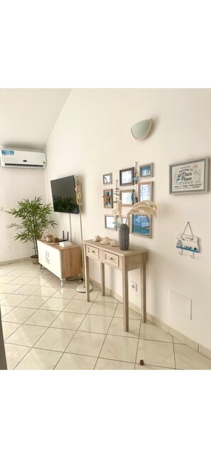 Ein Zimmer mit einem Flachbildfernseher, einem Holztisch, einer Topfpflanze und einer Wand-Klimaanlage.