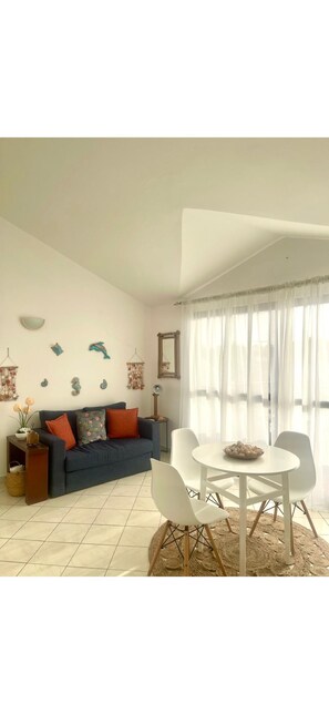 Ein Wohnzimmer mit einer Couch, einem Esstisch, Stühlen, einem Teppich und einem Fenster mit Vorhängen.