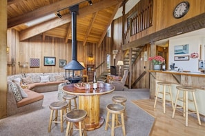 A wooden interior with a round wooden table, bar stools, a sofa, and a staircase.