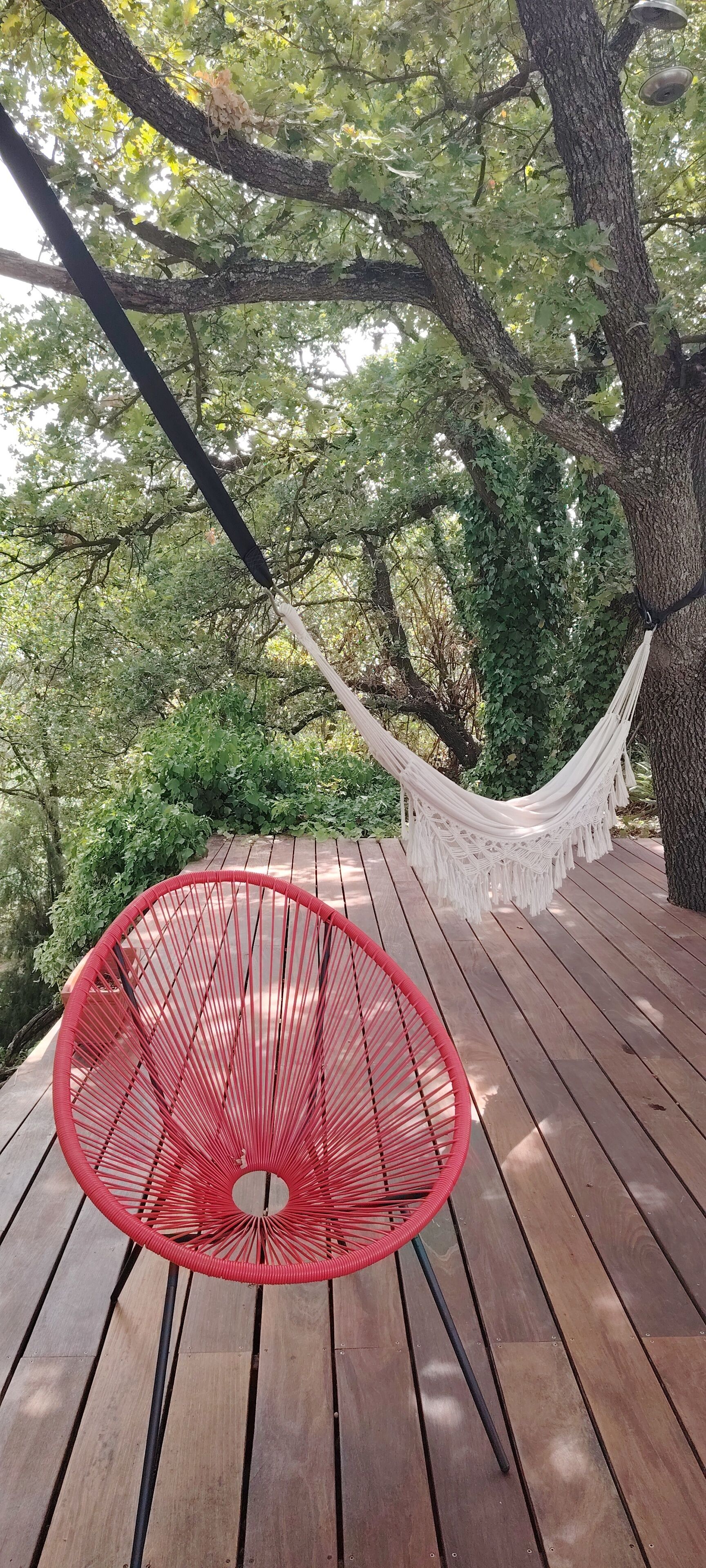 A hammock suspended between trees, a red chair, and a wooden deck.