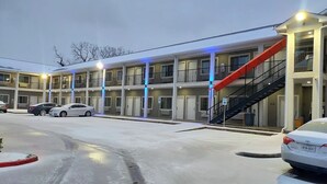 A multi-story motel with a parking lot, a red staircase, and a car parked in front. - Buzen Suites 2030 (Dallas)