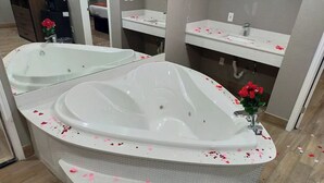 A bathroom with a large bathtub, a mirror, a sink, and a shower area. - Buzen Suites 2030 (Dallas)