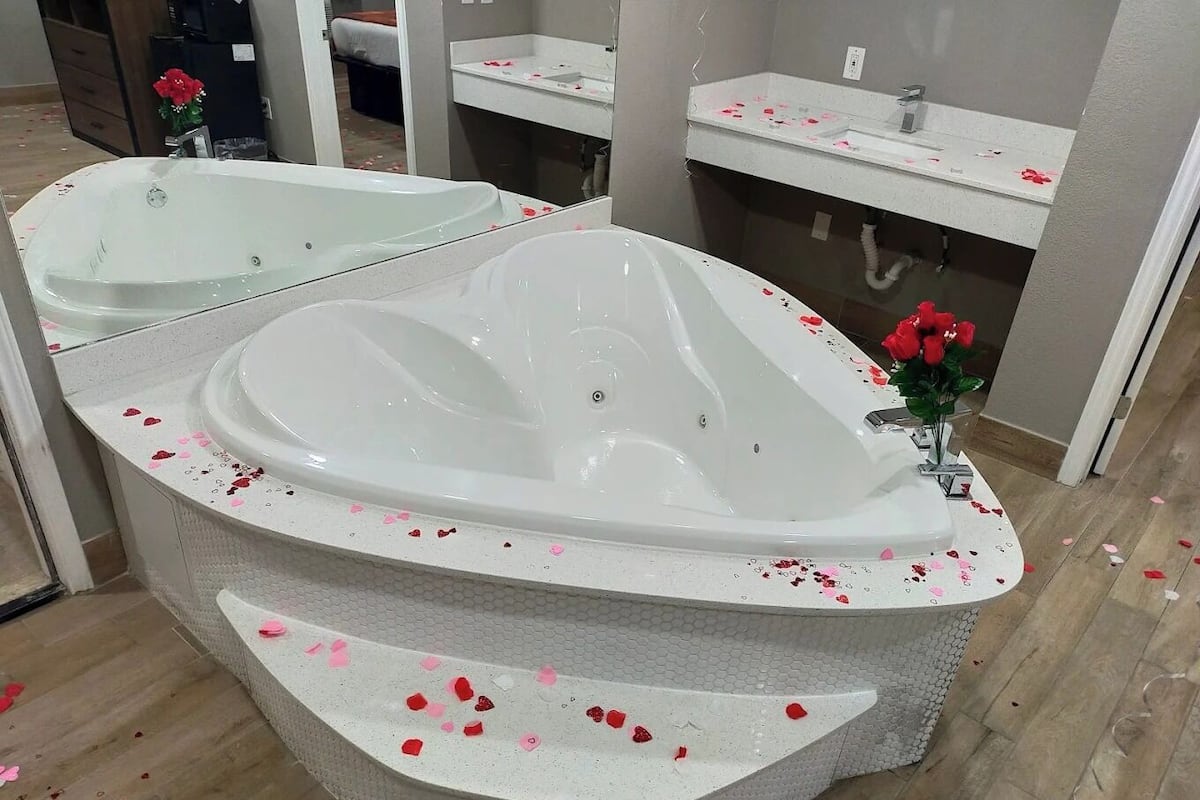 A bathroom with a large bathtub, a mirror, a sink, and a shower area.