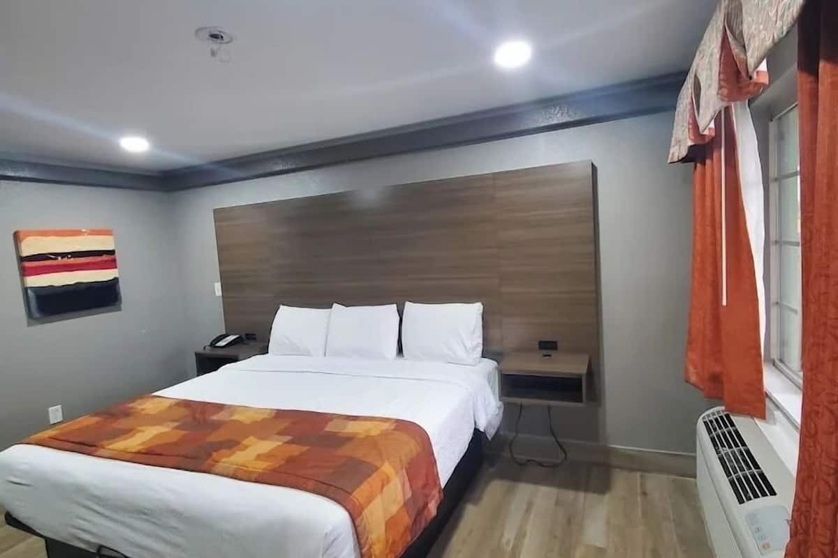 A hotel room with a bed, bedside table, wall art, and an air conditioning unit.