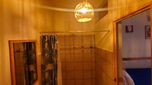 Un baño con ducha, un aplique colgante y una puerta que da a otra habitación.