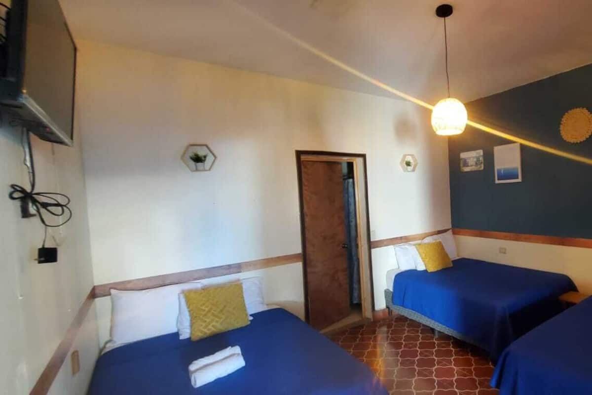 Quarto com duas camas, uma porta, televisão fixada na parede e iluminação no teto.