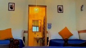 Habitación de hotel con dos camas, una araña, un lavamanos pequeño y una puerta que da a otra habitación.