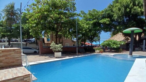Una piscina con borde de piedra, rodeada de árboles y un edificio al fondo.