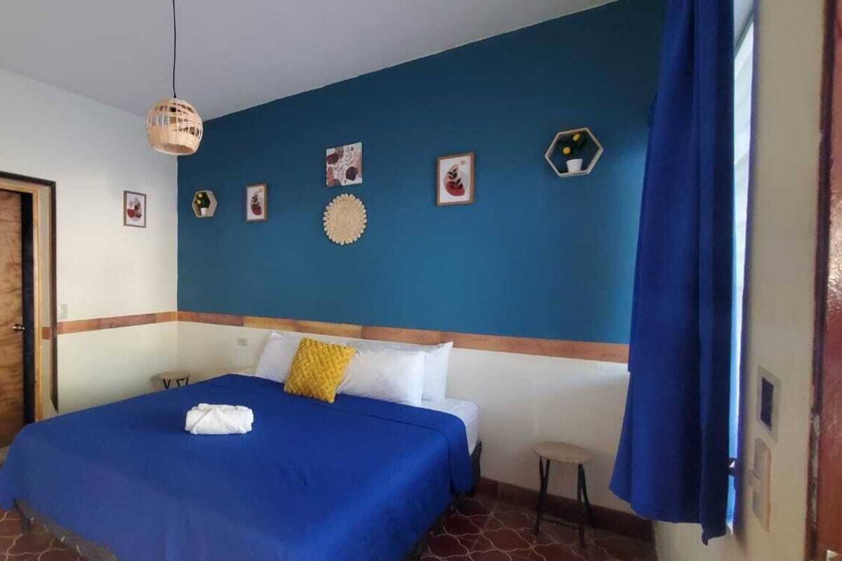 Quarto de hotel com cama, porta e parede azul com quadros.