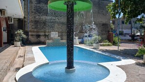 Una fuente con chorros de agua, una piscina y un muro de piedra al fondo.