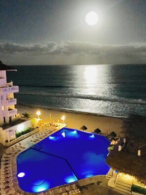 Ein Pool in Blautönen, Blick auf den Strand und ein Gebäude mit Balkonen.