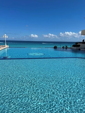 A clear blue pool with a view of the ocean and a lifeguard stand. - OCEAN FRONT APARTMENTS CANCUN (cancun)