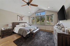 A bedroom with a large bed, a ceiling fan, a window with a view, and a dresser.