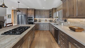 A modern kitchen with a central island, stainless steel appliances, wooden cabinets, and a marble countertop. - 7 bedroom Luxury by the Lake (South Lake Tahoe)