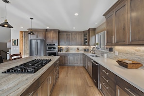 A modern kitchen with a central island, stainless steel appliances, wooden cabinets, and a marble countertop.