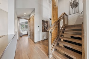 A wooden staircase with a railing, a hallway with wooden flooring, and a door leading to a room with a bed.