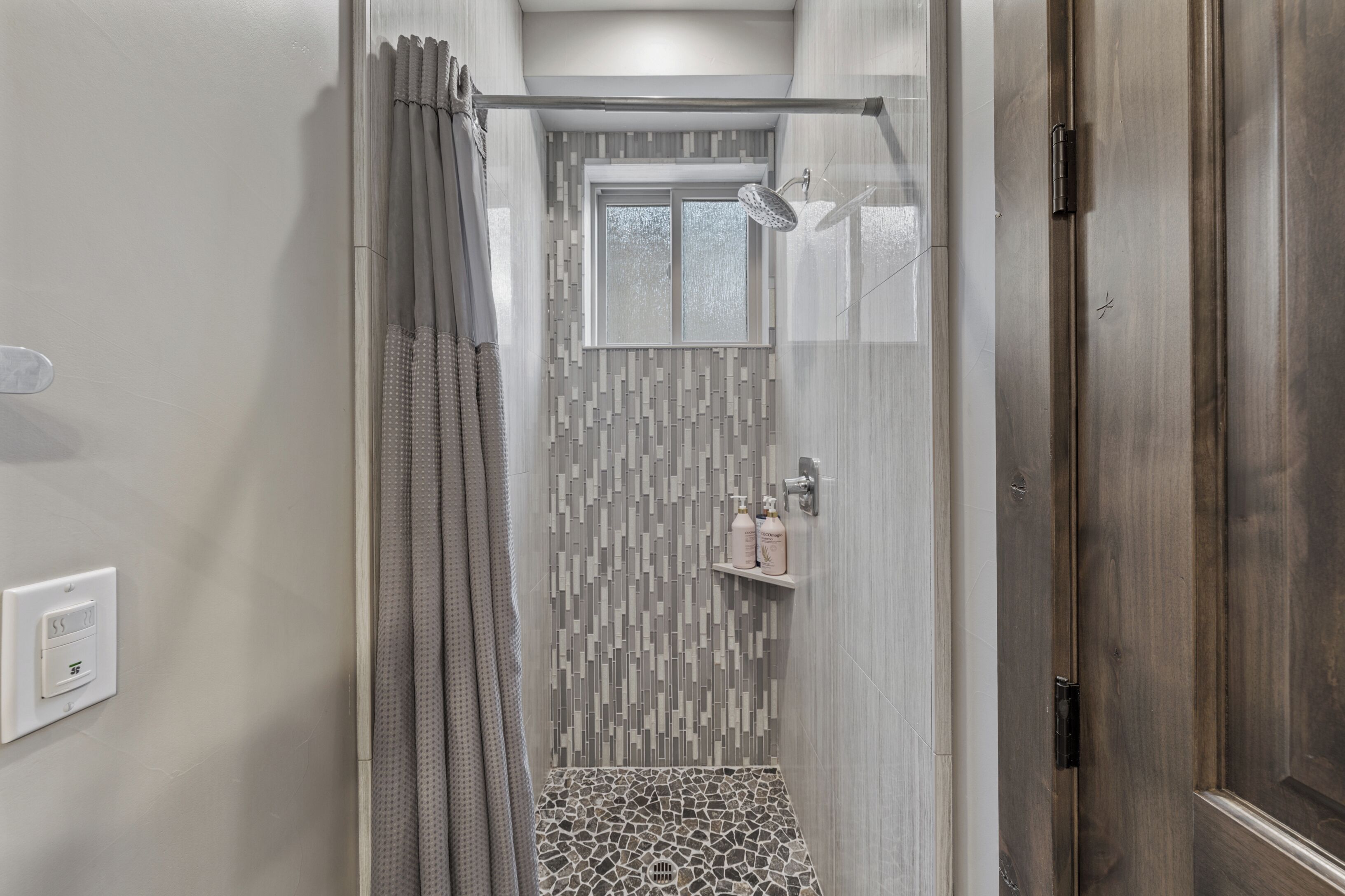 Una ducha con un revestimiento de pared estampado, una ventana y una puerta.