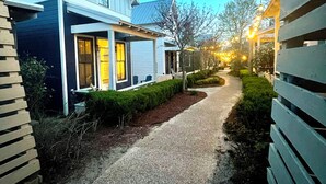 Uma entrada de automóveis residencial que leva a uma casa com varanda e luzes decorativas.