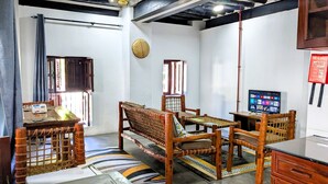 A room with a sofa, a television, a fire blanket, and a woven chair. - The Hub Train House Amazing Gents Code (Zanzibar Town)