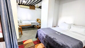 A room with a bed, a chair, a small table, and an air conditioning unit. - The Hub Train House Amazing Gents Code (Zanzibar Town)