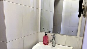 A bathroom with a white sink, a mirror, and a hand dryer. - The Hub Train House Amazing Gents Code (Zanzibar Town)