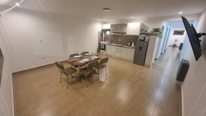 Una cocina moderna con armarios blancos, un comedor con mesa y sillas de madera, y un televisor de pantalla plana montado en la pared.