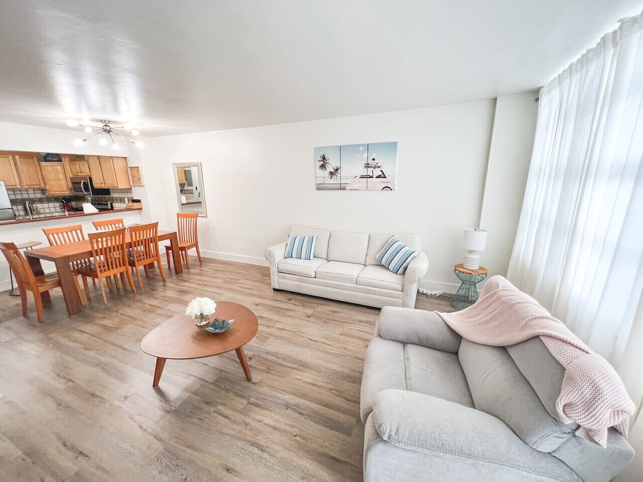 En stue med sofa, sofabord, spisebord og stole. Der er et køkkenområde med skabe og en mikrobølgeovn.