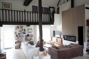 A spacious living area with a high ceiling, a staircase, a flat-screen TV, and a bookshelf. - Country house with exceptional view - sleeps 9/11 - swimming pool (Charny Orée de Puisaye)