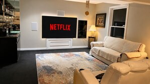Uma sala de estar com TV de tela plana, sofá, mesa de centro e estante de livros.