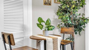 Un comedor con una mesa, sillas, una planta en maceta y dos cuadros en la pared.