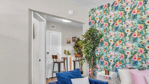 Un salón con un sofá azul, un sofá gris y un papel tapiz floral. Hay una puerta que da a otra habitación y una planta en la esquina.