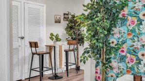 Un pasillo con puertas blancas, dos taburetes de bar, una mesa con una planta y una pared con estampado floral.