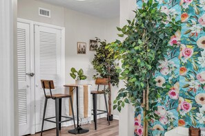 A hallway with white doors, two bar stools, a table with a plant, and a wall with a floral pattern. - Hidden Gem!  3BR Family home w/ Fire Pit & Games (St. Augustine)