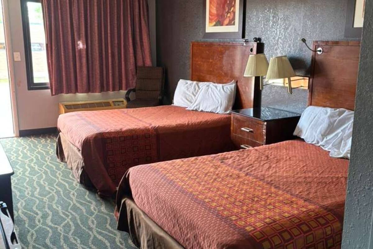 A hotel room with two beds, a desk, a chair, a window with curtains, and a painting on the wall.