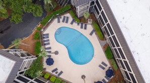 An aerial view of a swimming pool surrounded by lounge chairs and umbrellas, with a building in the background. - Oceanfront Escape • Steps to Sand • Walk to Coligny • South Forest Beach (Hilton Head Island)
