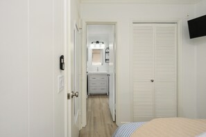 A bedroom with a bed, a wardrobe, a bathroom with a mirror and sink, and a TV mounted on the wall. - Oceanfront Escape • Steps to Sand • Walk to Coligny • South Forest Beach (Hilton Head Island)