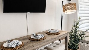 En matplats med ett långt träbord, bekväma sittbänkar, en platt-TV som är monterad på väggen och en lampa med flätad skärm.