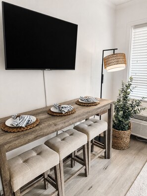 Ein Essbereich mit einem langen Holztisch, gepolsterten Bänken, einem wandmontierten Flachbildfernseher und einer gewebten Lampe.
