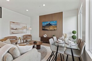 A modern living room with a glass dining table, sofas, and a large painting on the wall. - The Silo Park by Stylish Stays (Salt Lake City)
