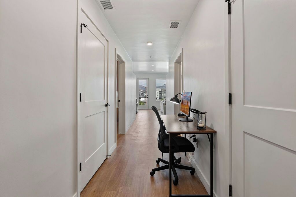 Un couloir étroit avec des portes blanches, un plancher en bois et un bureau sur lequel se trouvent un ordinateur et une lampe.