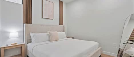 Un dormitorio con una cama grande, una mesita de noche, una lámpara de pared y un cuadro enmarcado.