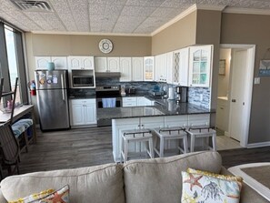 A modern kitchen with white cabinets, a stainless steel refrigerator, and a large island with bar stools. - Last minute discount for July 4th week 3-bedroom condo in North Wildwood (North Wildwood)