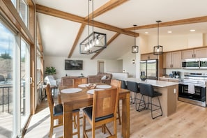 Una cocina amplia con electrodomésticos modernos, un comedor con mobiliario de madera y ventanas grandes con vistas.