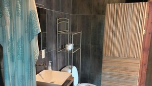 A bathroom with a wooden vanity, a white sink, a toilet, and a shower area with a wooden door. - BRISAMAR GUESTHOUSE (Puerto Escondido)