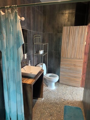 A bathroom with a wooden vanity, a white sink, a toilet, and a shower area with a wooden door. - BRISAMAR GUESTHOUSE (Puerto Escondido)