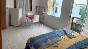 A bedroom with a bed, a desk with a chair, a fan, and a window. - BRISAMAR GUESTHOUSE (Puerto Escondido)
